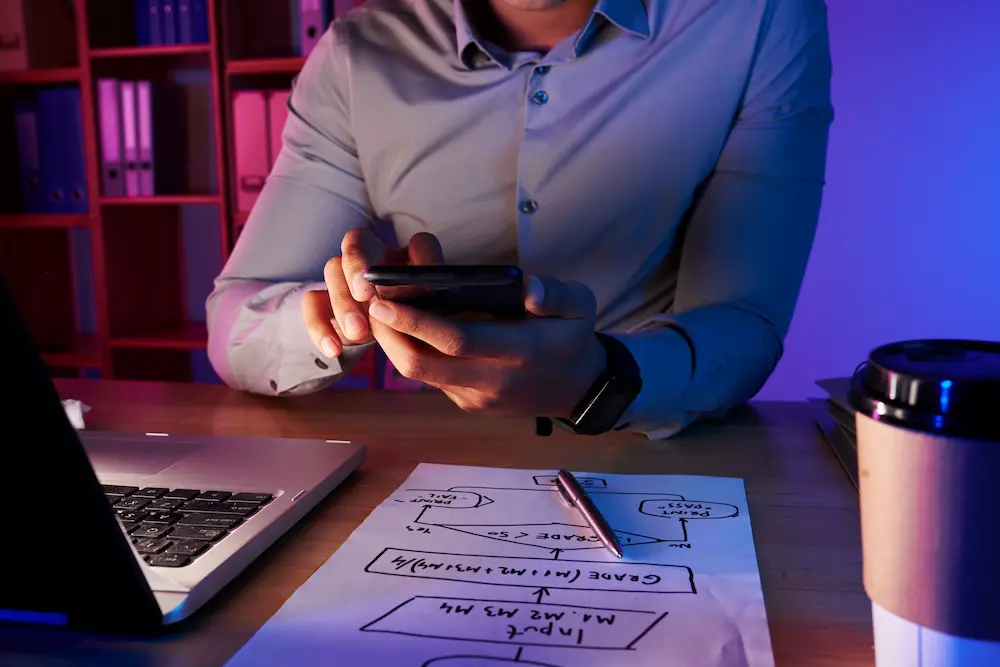 Persona revisando una idea de negocio en el celular junto a un esquema en papel, como metáfora de la necesidad de validar decisiones más allá de una respuesta de IA.